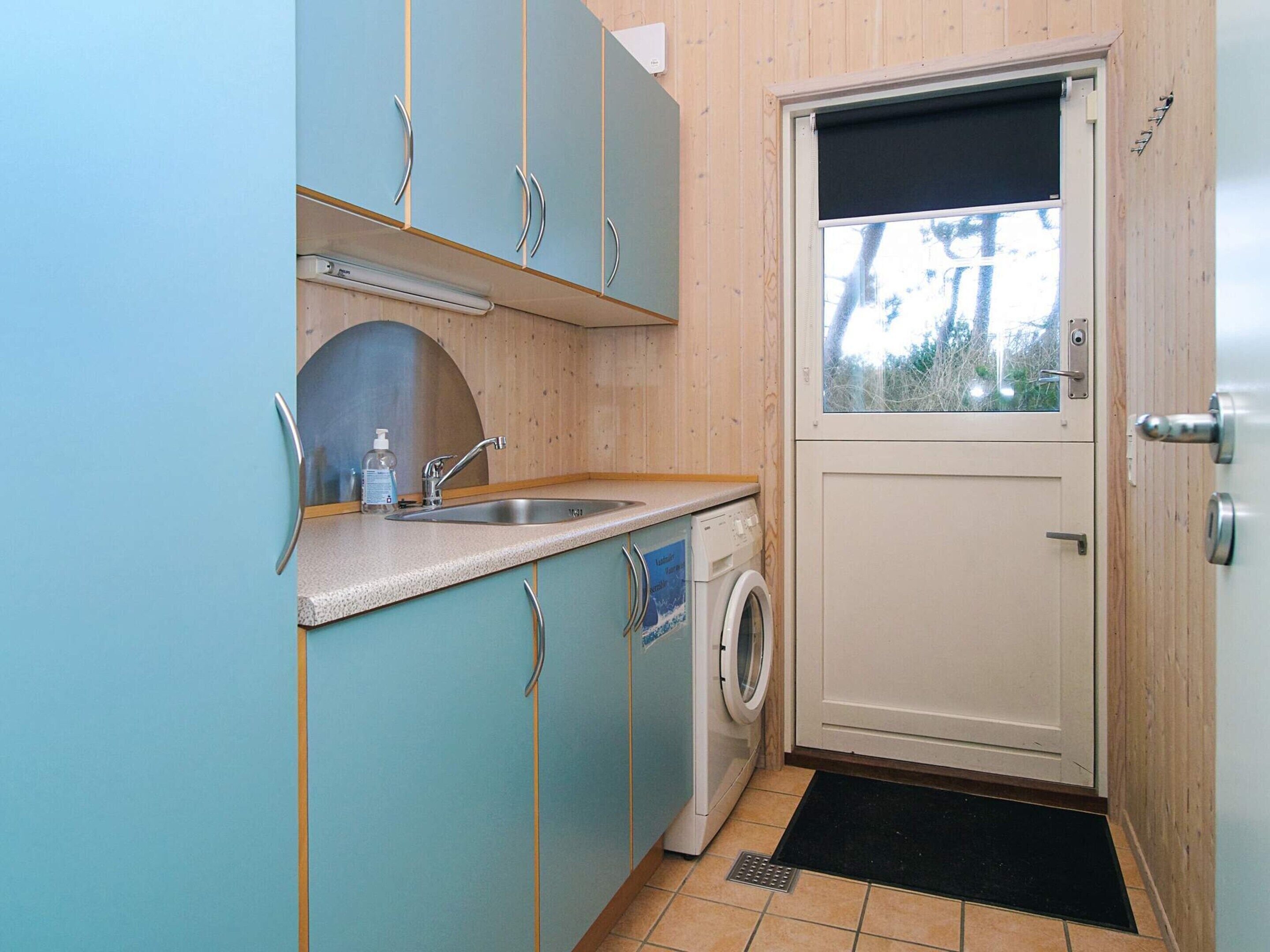 A compact kitchen with a washing machine, a sink, and a door with a window.