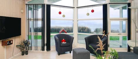 Una sala de estar moderna con un televisor grande, asientos cómodos y vistas al mar.