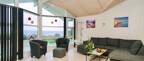 Uma sala de estar moderna com uma janela grande, um sofá, duas poltronas, uma mesa de centro e objetos decorativos.