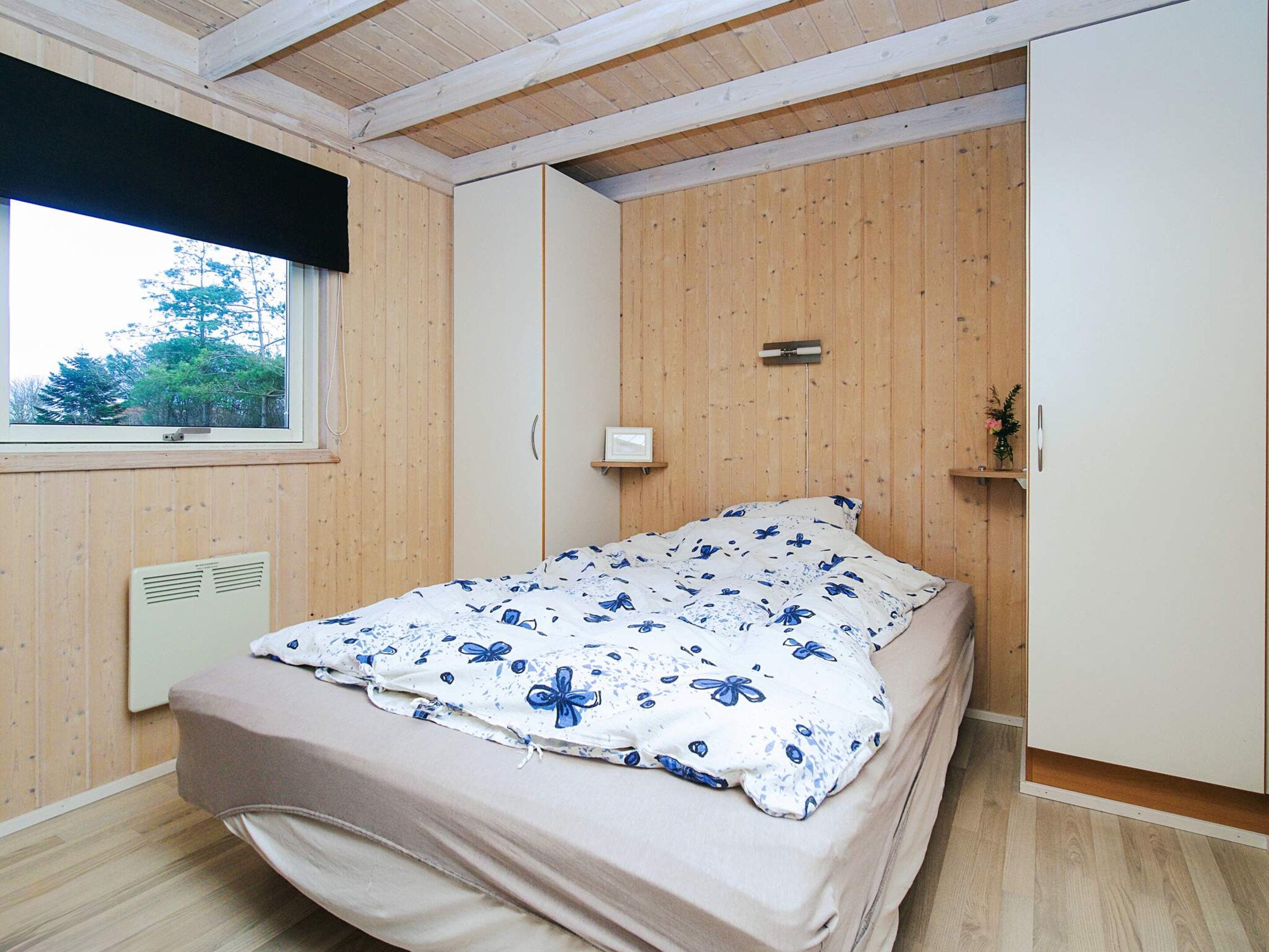 A bedroom with a bed, a window, a radiator, and wooden walls.