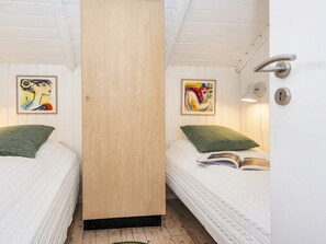 Une chambre avec deux lits simples, chacun agrémenté d’un oreiller vert et d’une couvre-lit blanche matelassée. Deux œuvres d’art encadrées ornent les murs, une porte dotée d’une poignée argentée et un luminaire au-dessus de la porte.