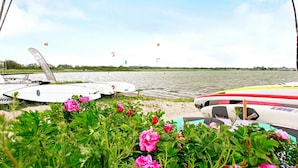 Vista sul lago con barche e aquiloni, circondata da vegetazione e fiori.