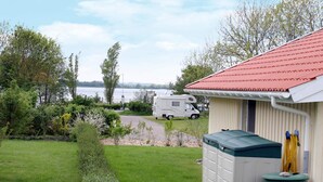Un terrain de camping pour caravanes avec une zone herbeuse, un petit abri et une étendue d’eau en arrière-plan.