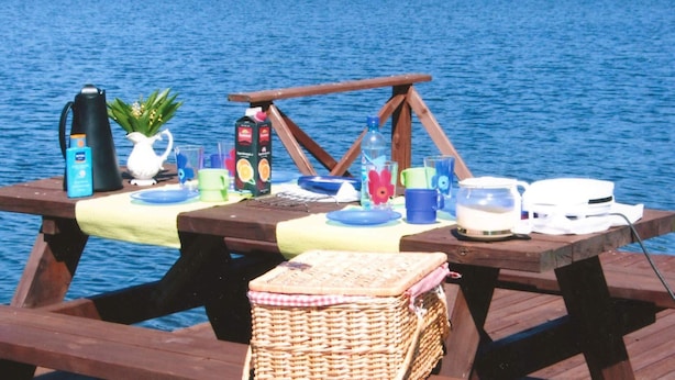 Et træborde til picnic ved en sø, med ting som en kedel, kopper og en kurv.