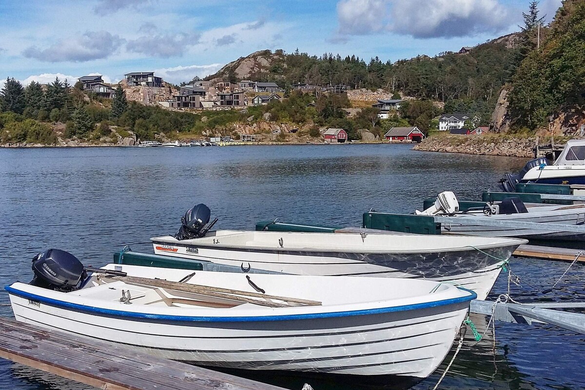 A row of small boats docked at a pier with a backdrop of houses and hills.
