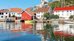 En havn med både og bygninger, herunder en rød og en gul båd fortøjet nær hvide huse med røde tage.