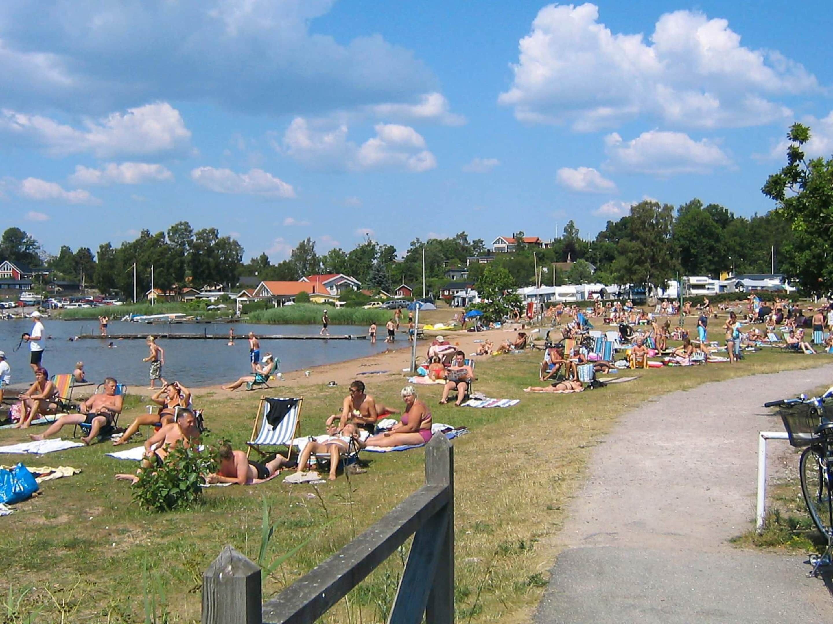 Un parque junto al lago, con gente relajándose sobre el césped y cerca del agua.