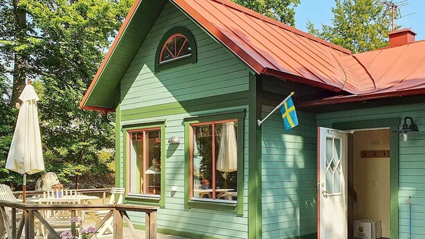 A green house with a red roof, a deck, and a flag.
