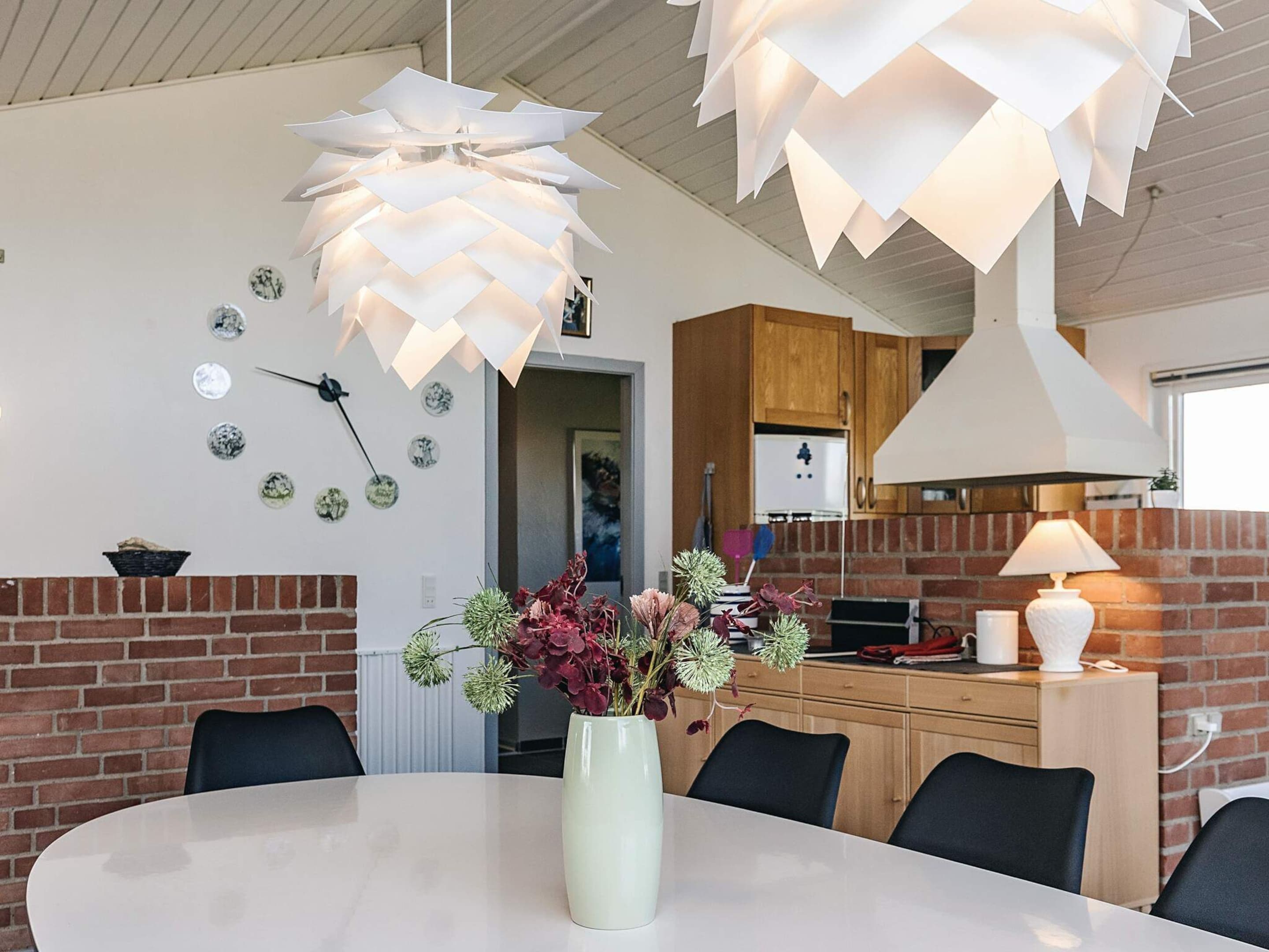 A modern dining area with a round table, a vase with flowers, and a unique ceiling light fixture.