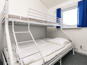 A bunk bed with a ladder, a window with blue curtains, and a white wall.
