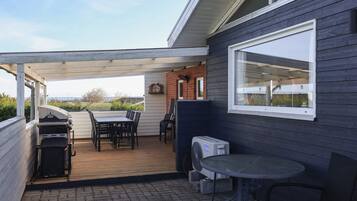 A covered patio area with a table and chairs, a grill, and a window.