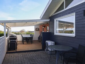 A covered patio area with a table and chairs, a grill, and a window. - 4 Star Holiday Home in Roslev (Roslev)