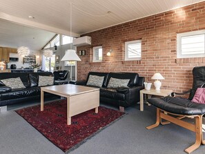 A modern living room with a brick wall, leather sofas, a coffee table, and a red rug.