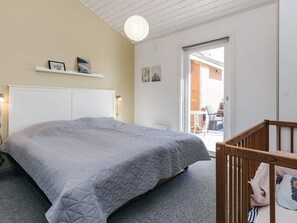 A bedroom with a large bed, a white headboard, a bedside lamp, a hanging light fixture, a small shelf with pictures, and a sliding glass door to a balcony. - 4 Star Holiday Home in Roslev (Roslev)