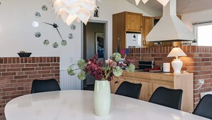 A dining area with a round table, chairs, a vase with flowers, and a modern pendant light.