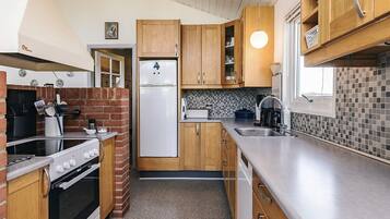 Eine kleine Küche mit Holzausbau, einem eingebauten Backofen, einem Kühlschrank und einer gefliesten Spritzschutzwand.