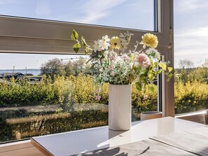 A window with a view of a river and houses, a white vase with flowers, and a table with a placemat.