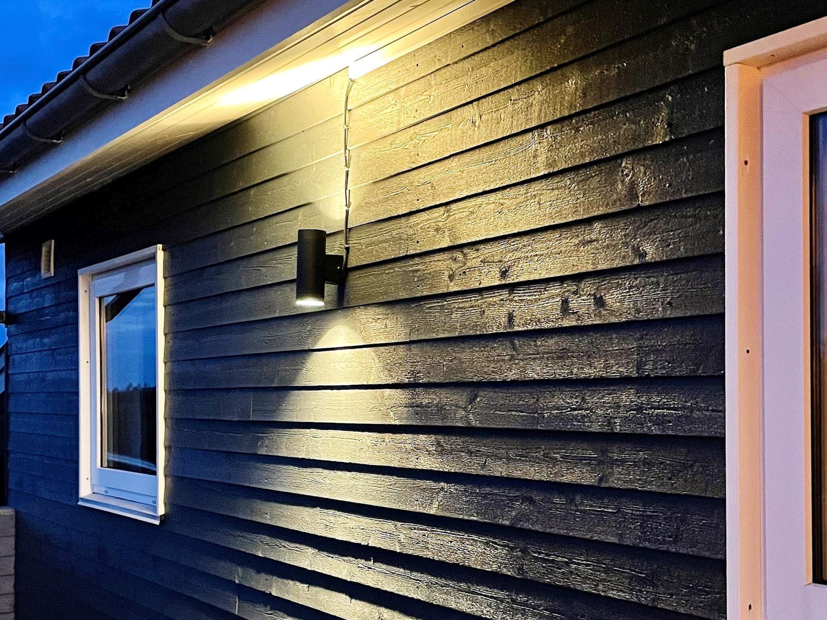 Un edificio con revestimiento horizontal, una ventana con marco blanco y un accesorio de luz fijado a la pared.