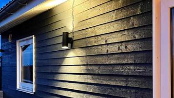 Un edificio con revestimiento horizontal, una ventana con marco blanco y un accesorio de luz fijado a la pared.