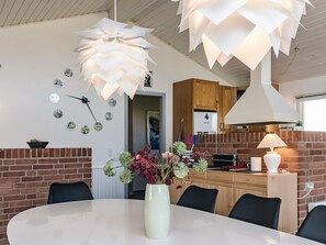 A modern dining area with a round table, chairs, a vase with flowers, and a unique ceiling light fixture. - 4 Star Holiday Home in Roslev (Roslev)