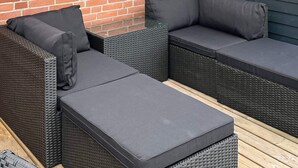A sectional outdoor sofa with cushions, a wicker frame, and a wooden deck.