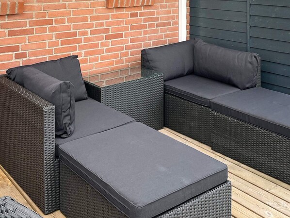 A sectional outdoor sofa with cushions, a wicker frame, and a wooden deck.