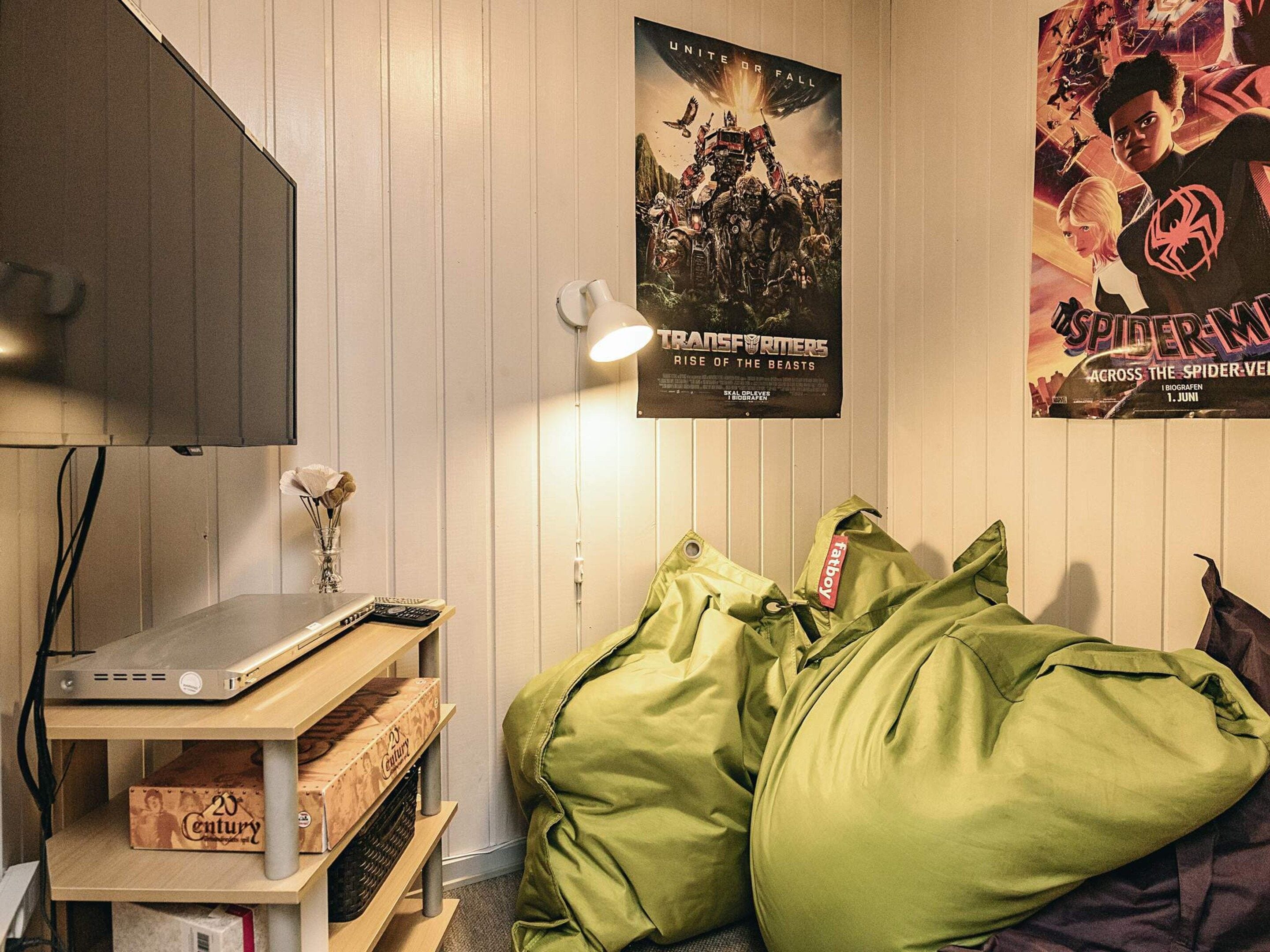 Una habitación con una cama, carteles en la pared, un escritorio con una computadora y una lámpara.