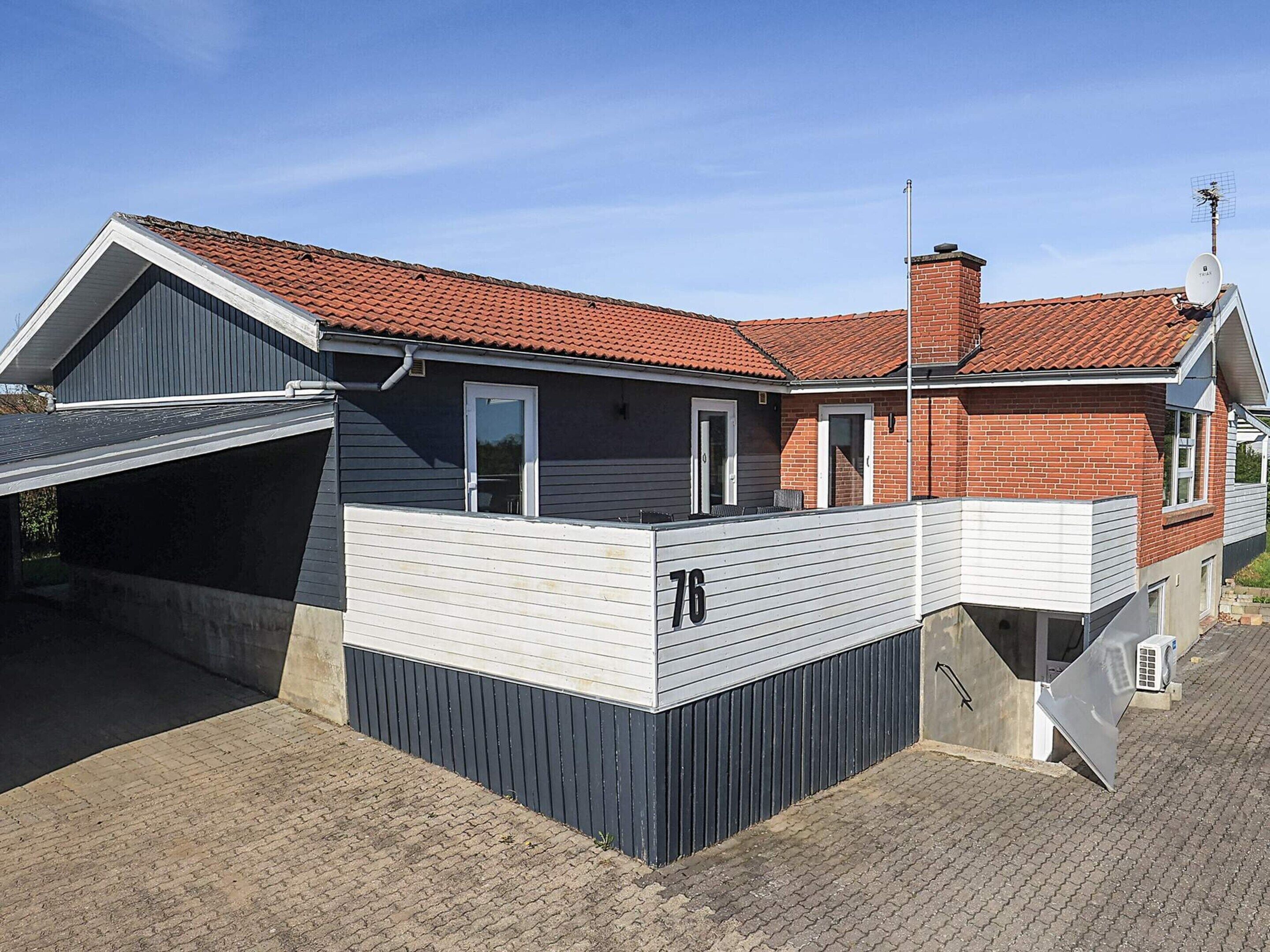 Ein modernes, zweistöckiges Haus mit rotem Ziegeldach, einer Garage und der Hausnummer 76.