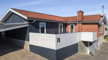 Ein modernes, zweistöckiges Haus mit rotem Ziegeldach, einer Garage und der Hausnummer 76.