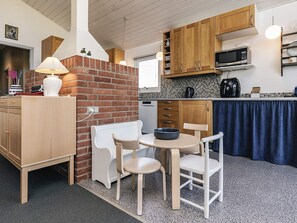 A compact kitchen with wooden cabinets, a microwave, a kettle, and a small dining table with chairs. - 4 Star Holiday Home in Roslev (Roslev)