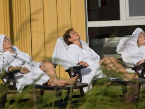 Three individuals in white bathrobes seated on lounge chairs outdoors. - Holiday Home in Otterndorf (Otterndorf)