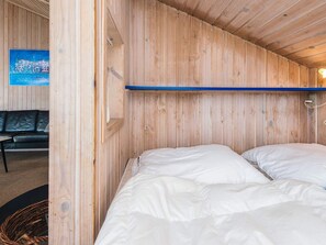 Una habitación con paneles de madera, una cama con ropa de cama blanca, un sofá de cuero negro y un estante azul.