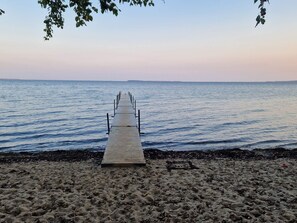 A wooden pier extending into calm waters with a sandy beach and distant land visible.