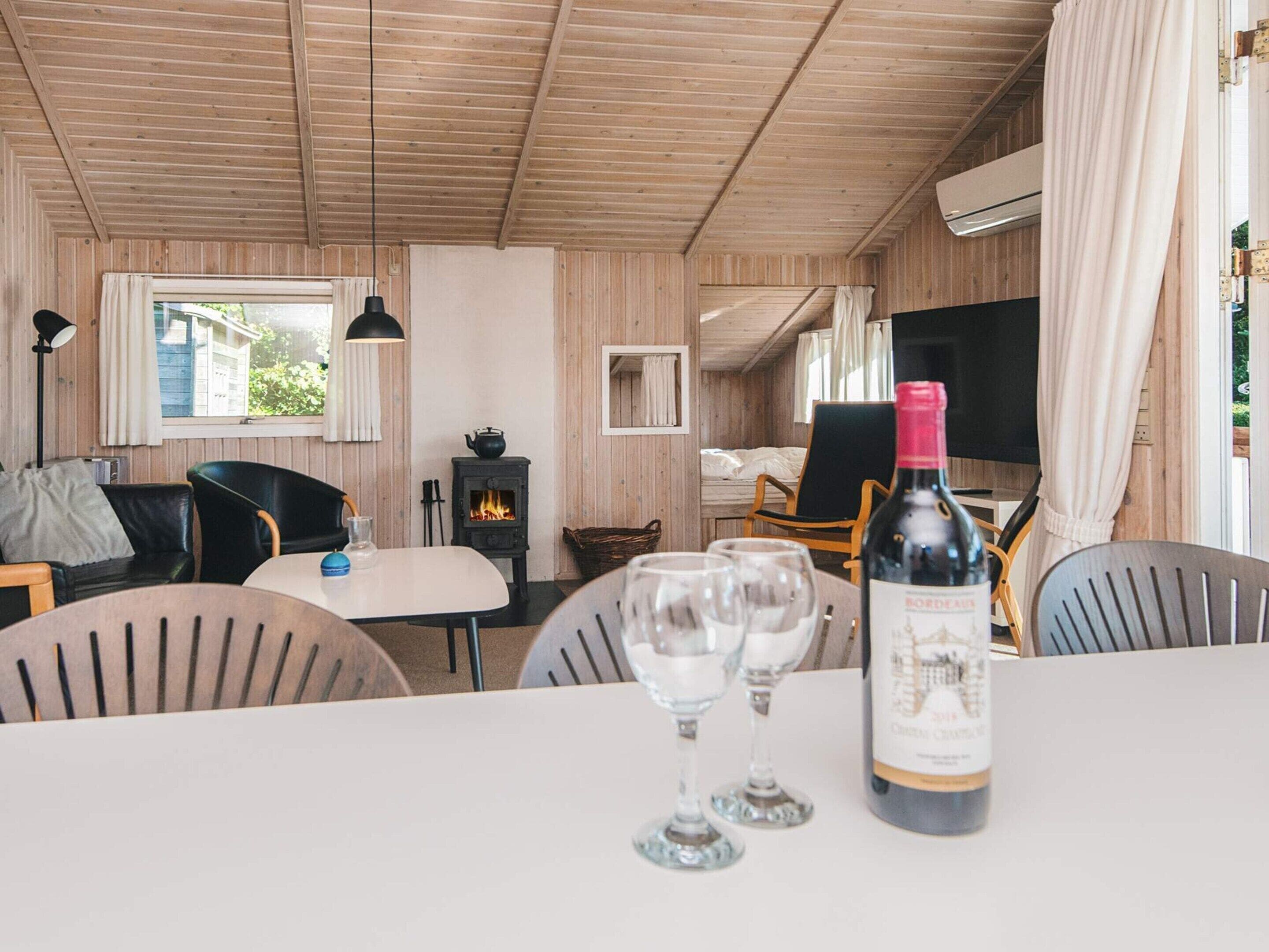 A cozy room with a wooden ceiling, a table with wine glasses, a bottle of wine, a TV, and a fireplace.