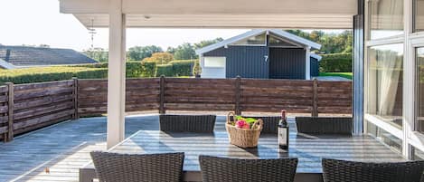 An outdoor patio with a table and chairs, a bottle of wine, and a basket of flowers.