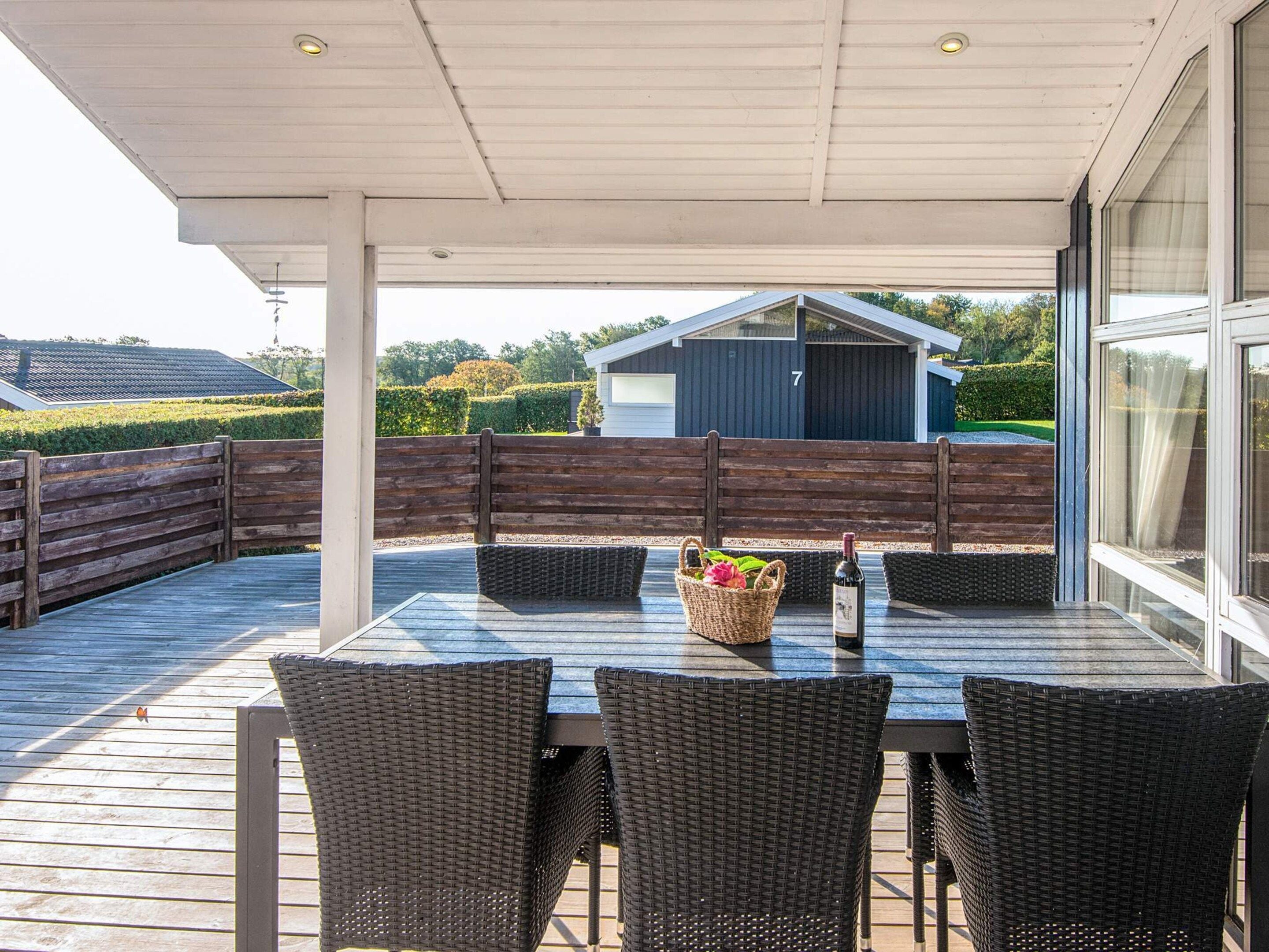 An outdoor patio with a table and chairs, a bottle of wine, and a basket of flowers.