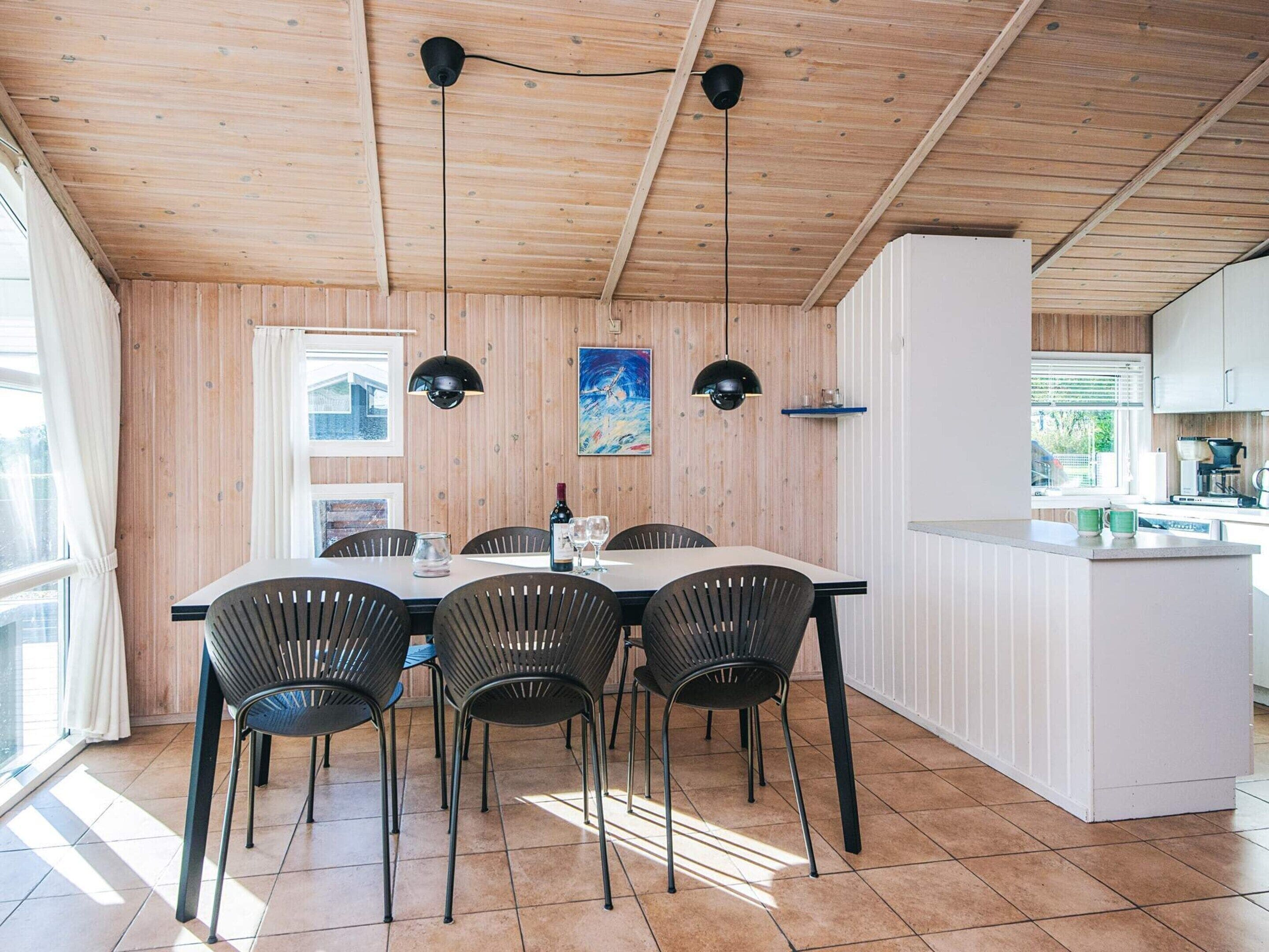 A dining area with a wooden ceiling, a white table, and black chairs. There are two pendant lights above the table.