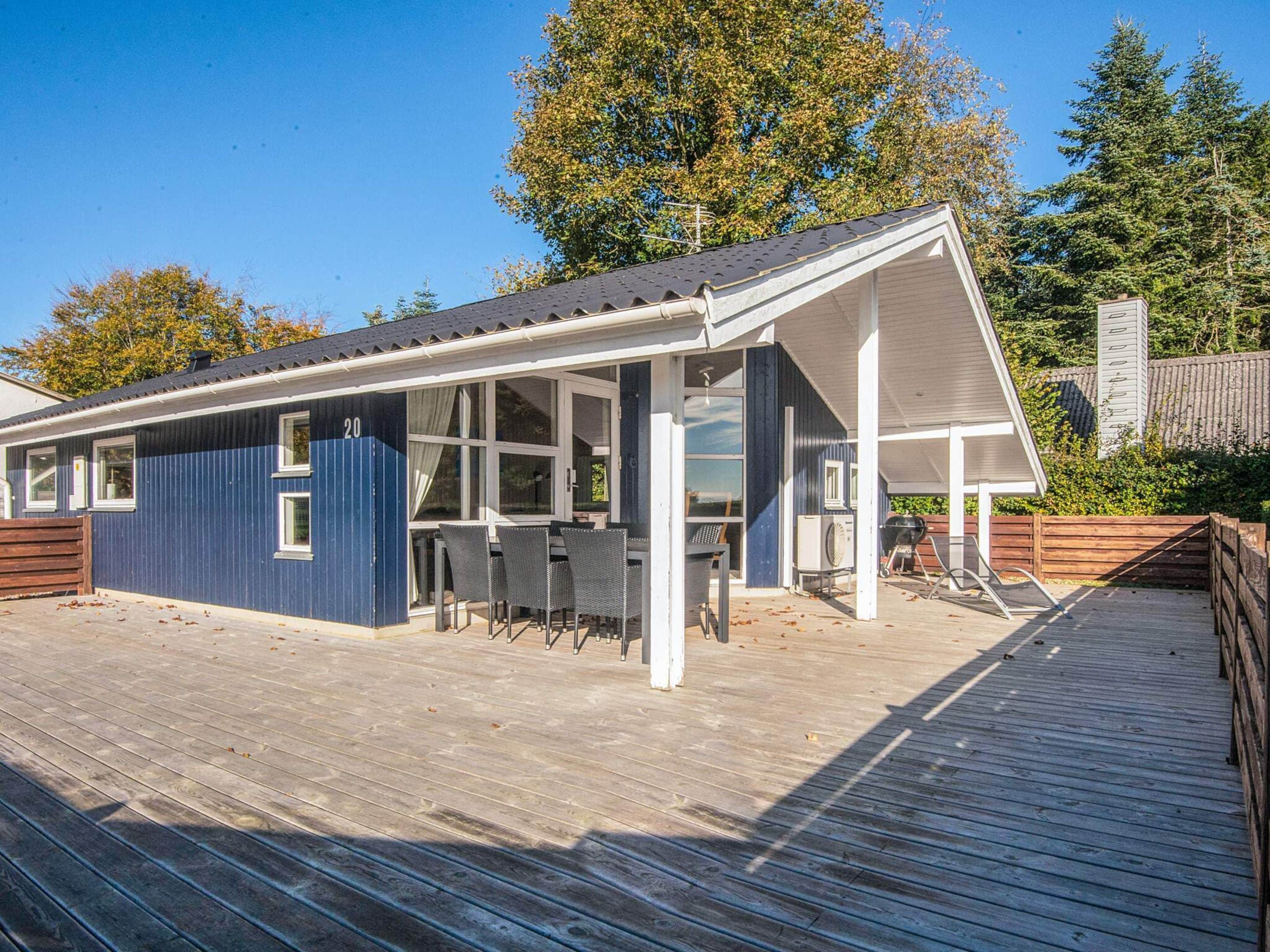 A covered outdoor area with a dining table and chairs, a barbecue grill, and a wooden deck.