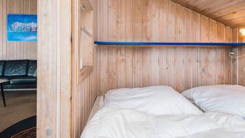 A room with a wooden wall, a bed with white bedding, and a black leather sofa.