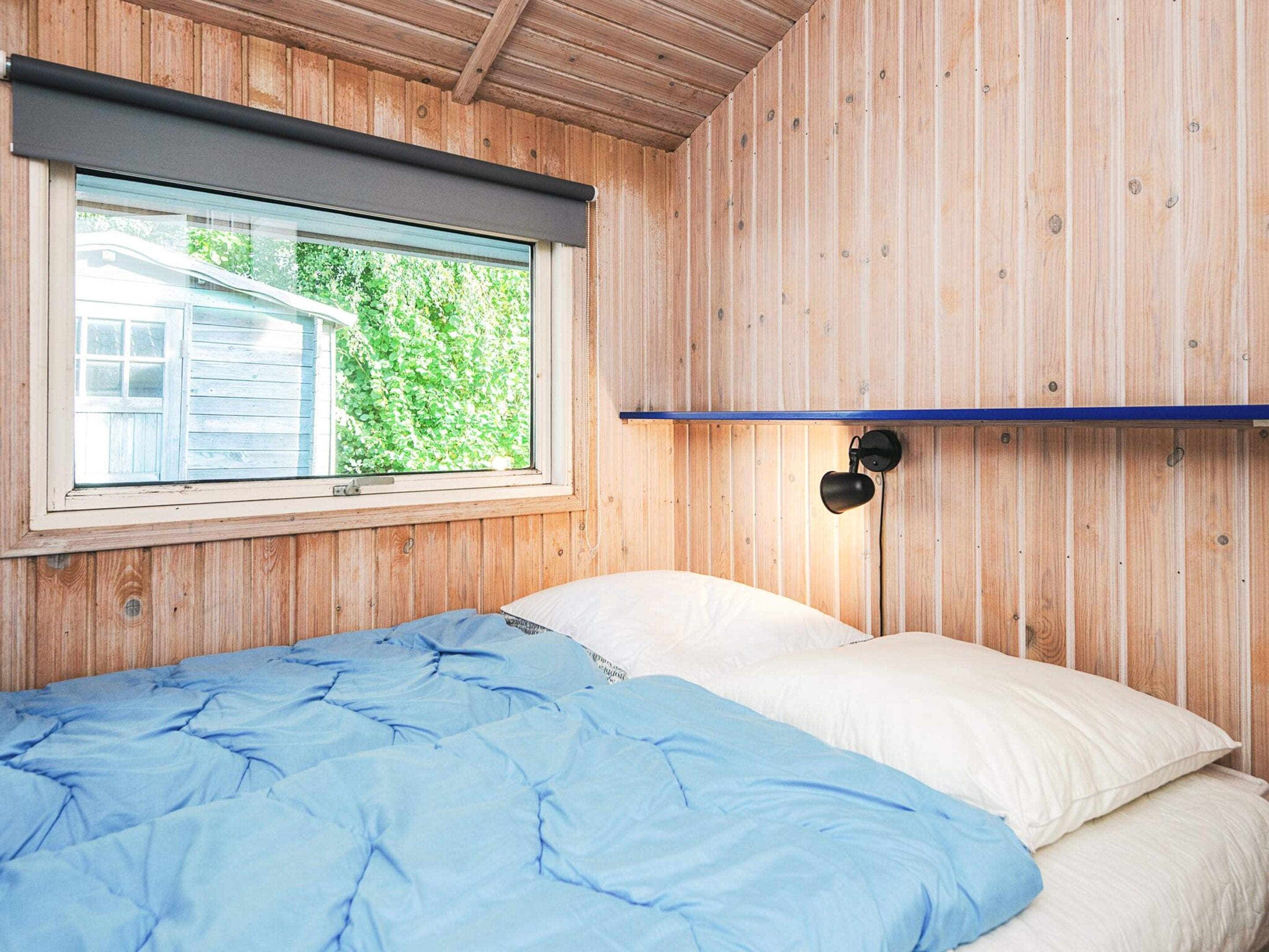 A room with a bed, a window, and a wall-mounted lamp.