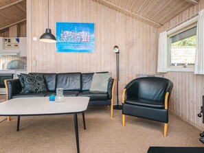 Une pièce chaleureuse avec un décor intérieur en bois, un canapé en cuir noir, un fauteuil en cuir noir, une table blanche et un tableau représentant un château.