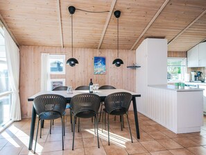 Un coin repas avec un plafond en bois, une table blanche et des chaises noires. Deux lampes suspendues sont placées au-dessus de la table.