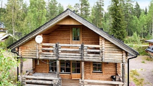 Une cabane en rondins avec un balcon, une porte d’entrée et des fenêtres.