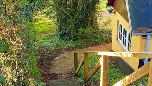 A wooden staircase leading to a yellow building with a window, surrounded by greenery. - 6 Person Holiday Home in Aabenraa (Aabenraa)