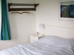 A bedroom with a bed, a bedside table with a lamp, a dresser, and a coat rack with hangers. - 6 Person Holiday Home in Aabenraa (Aabenraa)