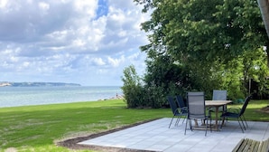An outdoor patio with a table and chairs, a wooden bench, and a view of the sea. - 6 Person Holiday Home in Aabenraa (Aabenraa)