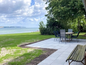 An outdoor patio with a table and chairs, a wooden bench, and a view of the sea. - 6 Person Holiday Home in Aabenraa (Aabenraa)