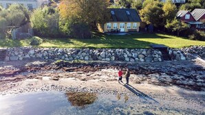 A coastal property with a stone wall, a grassy lawn, and a house in the background. - 6 Person Holiday Home in Aabenraa (Aabenraa)