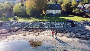 A coastal area with a stone wall, a grassy field, and a house in the background. - 6 Person Holiday Home in Aabenraa (Aabenraa)