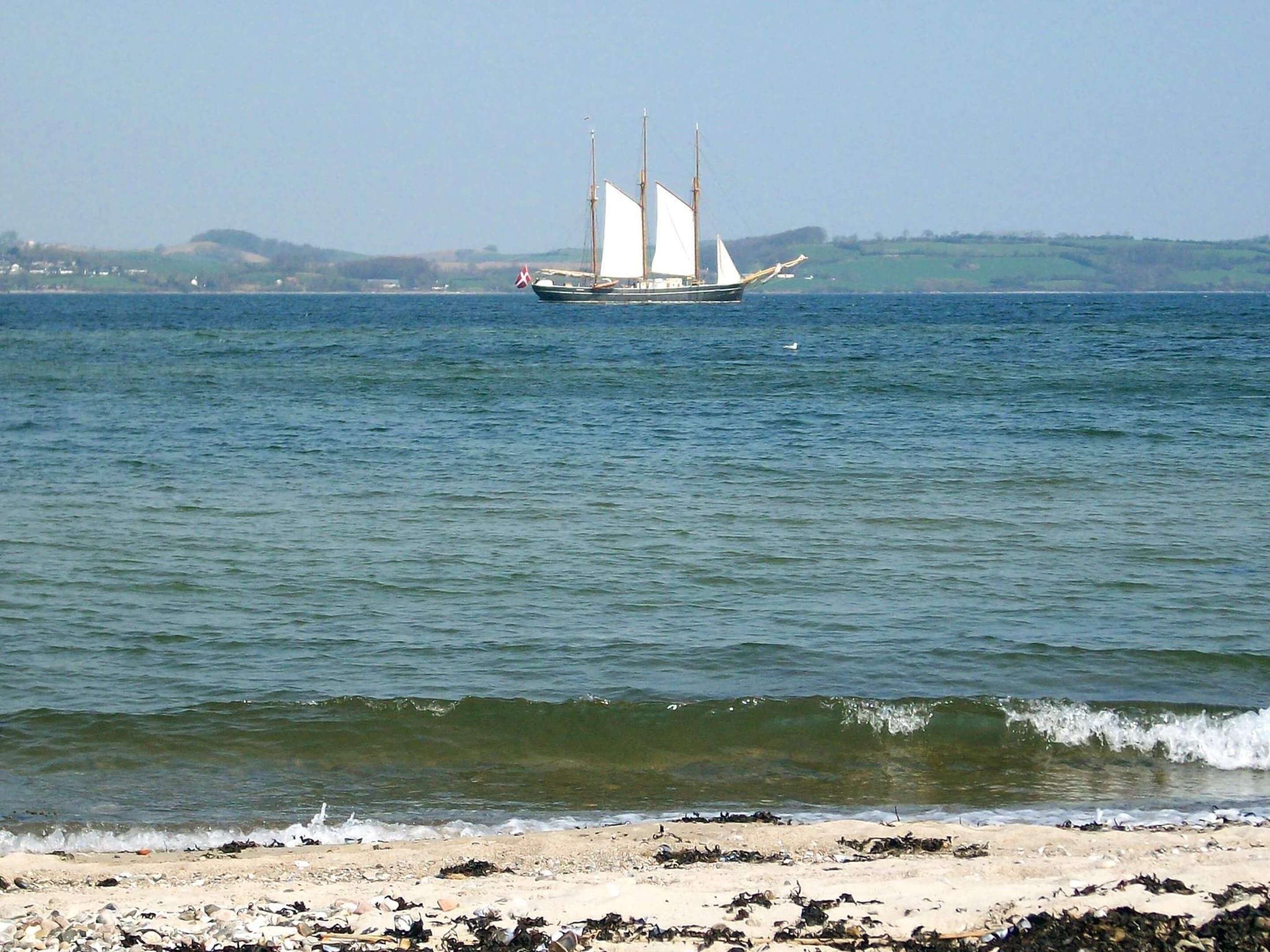 A sailboat on calm waters with a sandy beach in the foreground.